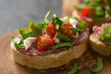 Bruschetta with mozzarella, cherry tomatoes and salame on olive board