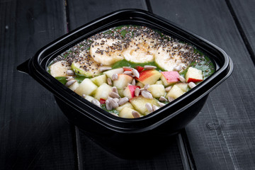 Porridge with fresh fruit and sunflower and sesame seeds in containers on a dark background. Takeaway. Diet and healthy food.