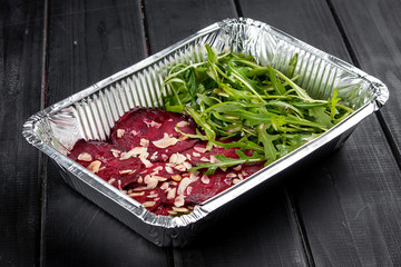 Beetroot carpaccio with peanut shavings and arugula in containers on a dark background. Takeaway. Diet and healthy food.