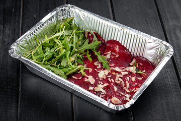 Beetroot carpaccio with peanut shavings and arugula in containers on a dark background. Takeaway. Diet and healthy food.