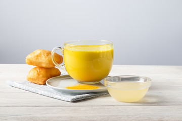 Golden milk with turmeric and honey, a traditional Indian drink on a white wooden background
