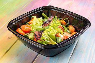 Salad with grilled salmon, lettuce and cherry tomatoes in containers on a colored wooden background. Takeaway. Diet and healthy food.