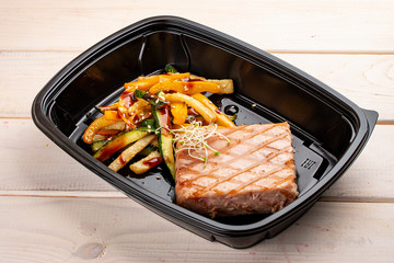Tuna steak with grilled vegetables in containers on a white wooden background. Takeaway. Diet and healthy food.