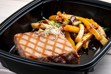 Tuna steak with grilled vegetables in containers on a white wooden background. Takeaway. Diet and healthy food.
