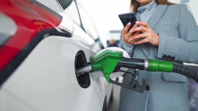 Woman using smartphone while her car is refueling. Slow motion