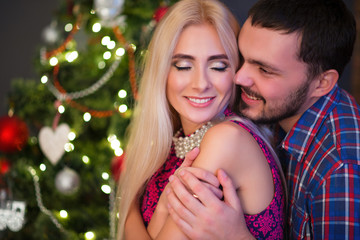 Man hugs his beautiful young wife over the shoulders during the New Year holidays at home. Traditional Holidays Concept