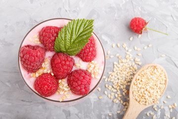 Yoghurt with raspberry and sesame in a glass and wooden spoon on gray concrete background. top view.