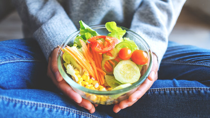 Closeup image of a woman holding a bowl of fresh mixed vegetables salad in hands