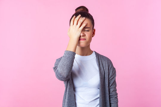 Facepalm, Oh No! Portrait Of Unhappy Teen Girl With Bun Hairstyle In Casual Clothes Standing With Hand On Head, Feeling Sorrow Regret Blaming Herself For Failure. Studio Shot Isolated, Pink Background