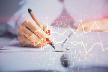 Double exposure of woman's hands making notes with forex graph hologram. Concept stock market analysis.