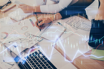 A woman hands writing information about stock market in notepad. Forex chart holograms in front. Concept of research. Double exposure