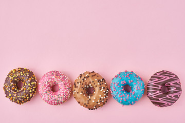 Different types of a colorful donats decorated sprinkles and icing on pastel pink background