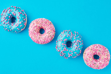 Different types of a colorful donats decorated sprinkles and icing on blue background