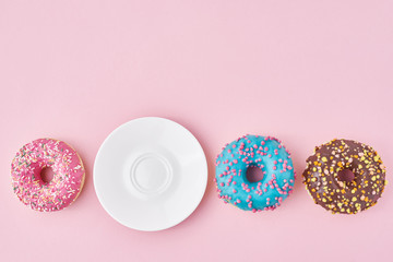 Different colorful donuts and empty plate on the pink background. Creative food concept