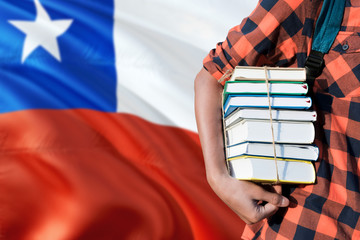 Chile national education concept. Close up of teenage student holding books under his arm with country flag background.