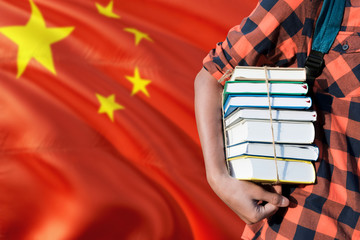 China national education concept. Close up of teenage student holding books under his arm with country flag background.