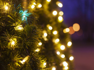 Photography of New Year lights on the fir with defocused background in night. Christmas mood, festive atmosphere. Suitable as template and background for postcards, greeting cards.