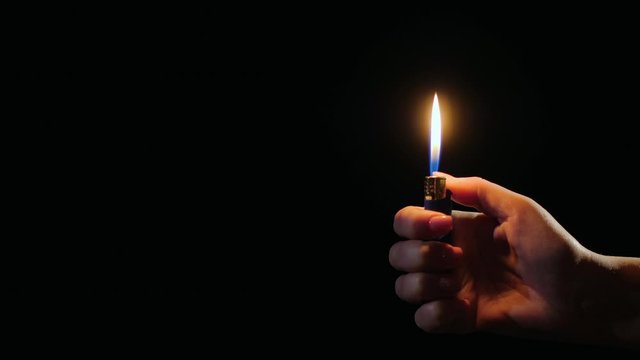 Hand ignites flames on lighter on black background