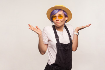 No idea. Portrait of confused clueless glamour hipster girl with violet hair in sunglasses and hat shrugging shoulders, doesn't know answer, uncertain puzzled expression. white background, studio shot
