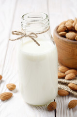 Obraz na płótnie Canvas Milk or yogurt in glass bottle on white wooden table with bowl of almonds on hemp napkin aside