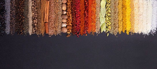 Seasoning, spice and herbs on black background with copy space. Panoramiс background with various condiments for food, top view - obrazy, fototapety, plakaty
