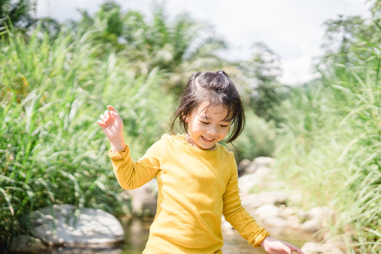 5 years old cute little girl playing in sunny summer river.Happy kid girl walking and playing in a forest near the river.Kids play outdoors.Kindergarten in school travel on summer day.