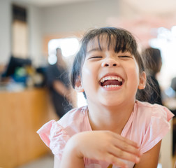 Happy Little asian girl child showing front teeth with big smile and laughing in restaurant, she...