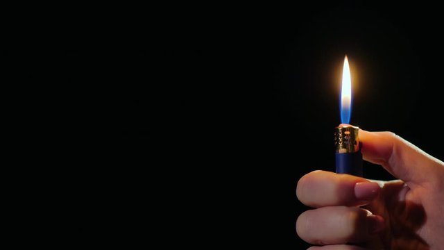Hand ignites flames on lighter on black background