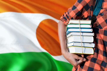 Niger national education concept. Close up of teenage student holding books under his arm with country flag background.