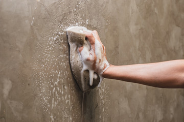 Men's hands are using a sponge cleaning on the concrete wall.
