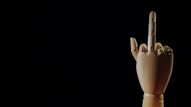 Wooden hand shows obscene gesture with middle finger on black background