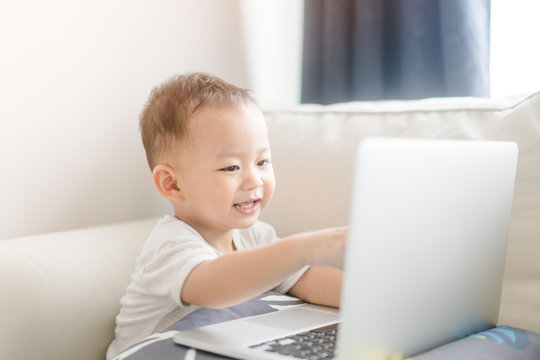 Portrait of a little toddler boy watching laptop and exciting face.Little asian boy child with laptop computer or notebook in living room at home.E Learning, Shopping online concept.