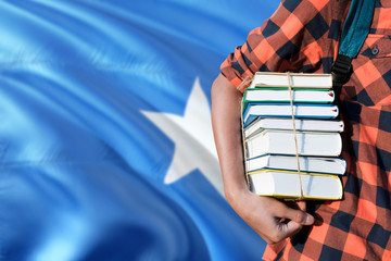 Somalia national education concept. Close up of teenage student holding books under his arm with country flag background.
