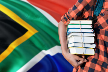 South Africa national education concept. Close up of teenage student holding books under his arm with country flag background.