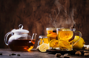 Winter or autumn hot healing tea with ginger, honey, lemon and spices in glass cup with steam, rustic wooden background