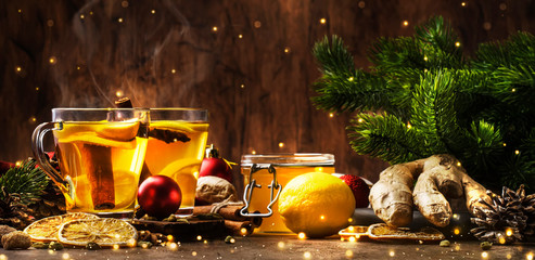 Winter hot tea with fruit, lemon and spices in glass cup with steam in Christmas or New Year's table setting, rustic wooden background