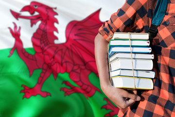 Wales national education concept. Close up of teenage student holding books under his arm with country flag background.