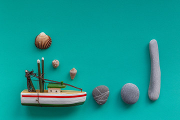 Little boat with stones and sea shells on green background