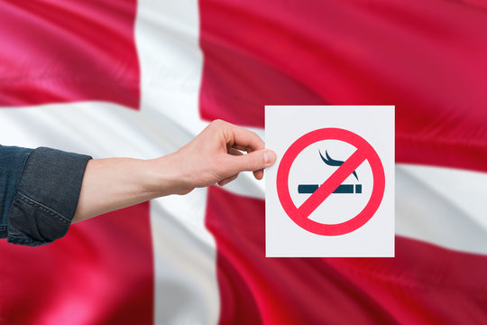 Denmark health concept. Hand holding paper with no smoking sign over national waving flag. Quit smoke theme.