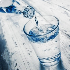 Nalewanie wody do szklanki z butelki ze szkła - obrazy, fototapety, plakaty