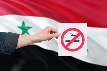 Syria health concept. Hand holding paper with no smoking sign over national waving flag. Quit smoke...