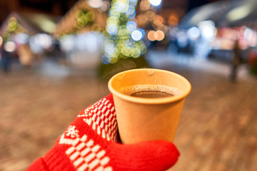 Hand holding a cup of mulled wine with blurred background of winter wonderland, a Christmas Market...