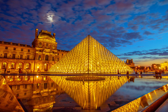 Paris, France - July 1, 2017: twilight reflections around Louvre Museum glass pyramid. Louvre palace in the courtyard. Picture gallery landmark hosting Mona Lisa painting by Leonardo Da Vinci.
