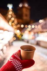 Hand holding a cup of mulled wine with blurred background of winter wonderland, a Christmas Market in European small city