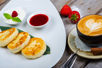 Traditional breakfast with coffee and cheesecakes, cottage cheese pancakes on a plate with syrup and jam.