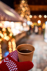 Hand holding a cup of mulled wine with blurred background of winter wonderland, a Christmas Market in European small city