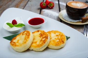 Traditional breakfast with coffee and cheesecakes, cottage cheese pancakes on a plate with syrup and jam.