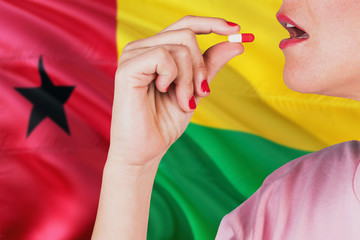 Guinea Bissau health care concept. Close-up of a woman taking vitamin capsule on national flag background.
