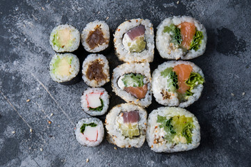 Different sushi on a dark textured background, fresh futomaki, uramaki and hosomaki.