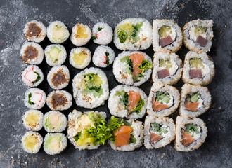 Different sushi on a dark textured background, fresh futomaki, uramaki and hosomaki.